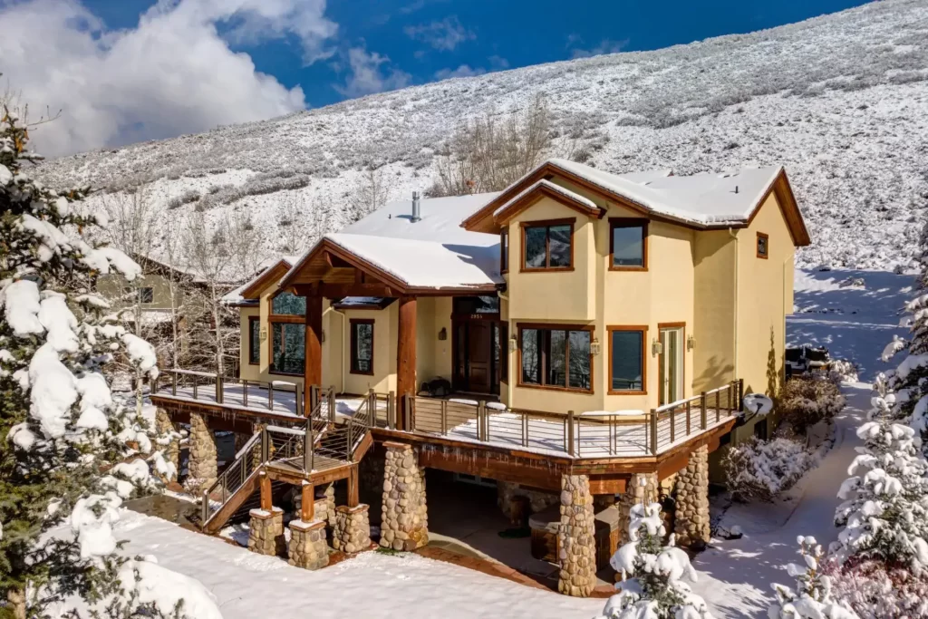 Large two-story yellow home covered in snow on a hillside